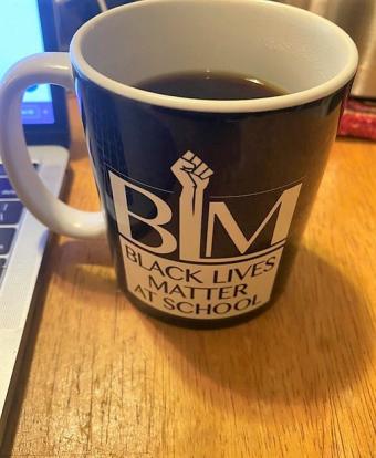 image of a coffee cup that says "black lives matter at schools" next to a laptop on top of a desk